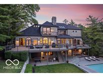 Stunning multi-level stone home with large deck, lush landscaping, and beautiful sunset backdrop at 11715 Landings Dr, Indianapolis, IN 46256