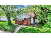 Charming single-story home featuring brick accents, a cozy front porch, and mature trees in a lush green lawn at 1523 E Mills Ave, Indianapolis, IN 46227