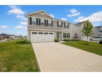 Two-story home featuring a two-car garage, tan siding, black shutters and a well-maintained green lawn with a long driveway at 13887 N Hawkers Hill Dr, Camby, IN 46113