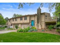 Two-story townhome with a stone chimney, a stone facade, attached garages, a deck, and a vibrant blue front door at 7831 Eagle Valley Pass, Indianapolis, IN 46214