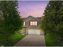 Charming two-story brick home with a well-manicured lawn and attached two-car garage at dusk at 8631 Belle Union Pl, Indianapolis, IN 46113