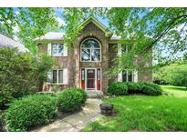 Charming two-story brick home with lush landscaping, bright green lawn, and a welcoming red front door at 50 Charing Cross Rd, Indianapolis, IN 46217