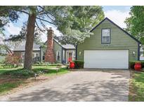 Exterior view of a charming green home with white garage door, red door and mature trees at 6210 Mckinley Ct, Indianapolis, IN 46220