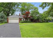 Charming brick home featuring an attached two-car garage, lush green lawn, mature trees, and professionally landscaped garden at 8752 Washington Blvd E Dr, Indianapolis, IN 46240
