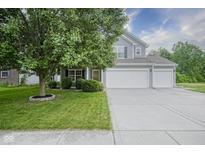 Well-maintained two-story home with a three-car garage and lush green lawn and beautiful tree at 13817 Black Canyon Ct, Fishers, IN 46038