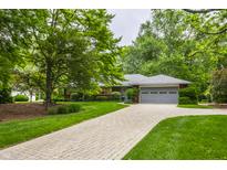 Charming home featuring a brick exterior, grey roof, lush greenery, and a paved driveway at 8905 Washington Blvd West Dr, Indianapolis, IN 46240