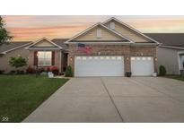 Charming brick home featuring an attached two car garage, manicured lawn, and an American flag at 1468 Blackthorne N Trl, Plainfield, IN 46168