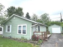 Charming single-story home features a light green exterior, wooden deck, and a detached garage, offering a cozy and inviting curb appeal at 1801 Bauer Rd, Indianapolis, IN 46218