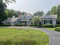 Stately gray home with an American flag, circular driveway, and well-manicured lawn and landscaping at 9510 Copley Dr, Indianapolis, IN 46260