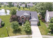 Beautiful brick home featuring mature landscaping, a spacious driveway, and picturesque pond views at 14353 Chariots Whisper Dr, Carmel, IN 46074