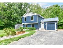 Charming blue two-story home with a well-maintained lawn and a detached garage surrounded by lush trees at 1513 Alimingo Dr, Indianapolis, IN 46260