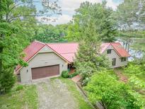 Charming home features a red roof, attached garage, and is surrounded by lush greenery and a view of the lake at 5821 Bittersweet Rd, Morgantown, IN 46160