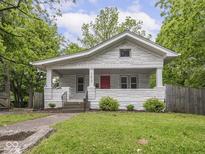 Charming bungalow with a red front door, white brick facade, and landscaped front yard, surrounded by mature trees at 1617 E 52Nd St, Indianapolis, IN 46205