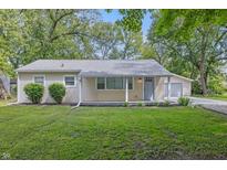 Charming single-story home featuring a light yellow exterior, well-manicured lawn, and a detached garage nestled among mature trees at 420 Vista Dr, Carmel, IN 46280