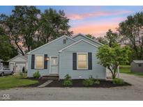 Charming single-story home featuring light blue siding, dark shutters, and manicured front garden under a colorful dusk sky at 604 Alexandria Pike, Anderson, IN 46012