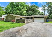 Stone ranch home featuring a two-car garage, mature trees, and a stone wall surrounding the front yard at 741 Fairway Dr, Indianapolis, IN 46260