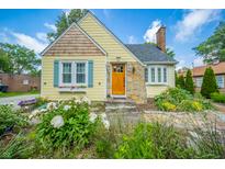 Charming yellow home featuring stone accents, a welcoming wooden front door, and lush landscaping at 311 Northshore Blvd, Anderson, IN 46011