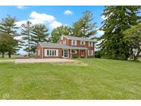 Two-story brick home with an expansive lawn, mature trees, and red front door offers classic charm and curb appeal at 4817 N 150 W, Anderson, IN 46011