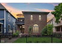 Charming brick home featuring a balcony, arched windows, and a well-manicured lawn with black fence at 1436 Central Ave, Indianapolis, IN 46202