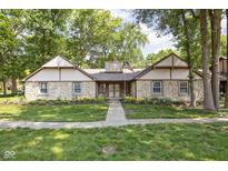 Charming stone home featuring mature trees, manicured lawn and a traditional American flag display at 2947 Talping Row, Indianapolis, IN 46268
