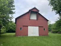 Red barn with white sliding doors and two windows is surrounded by a lush green lawn and trees at 18229 Moontown Rd, Noblesville, IN 46062