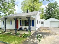 Charming single-story home features a red front door, blue shutters, decorative porch columns, and a detached garage at 828 N Clarkdale Dr, Muncie, IN 47304