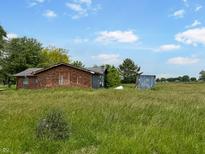 A single-story red brick home set on a lot with overgrown grass under a blue sky at 2074 W 300 S, Shelbyville, IN 46176