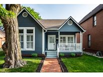 Charming blue home featuring a quaint front porch, manicured lawn, and a classic brick walkway at 608 E 9Th St, Indianapolis, IN 46202