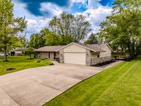 Charming single-story home featuring stone accents, a two-car garage, and a long driveway with lush landscaping at 7405 N Janna Dr, Muncie, IN 47303