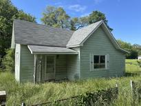 Quaint exterior view of a home with weathered siding and an overgrown yard under a blue sky at 1739 E 18Th St, Anderson, IN 46016