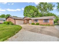 Single story brick home featuring an attached garage, concrete driveway, and lush green landscaping at 407 Woodland E Dr, Greenfield, IN 46140