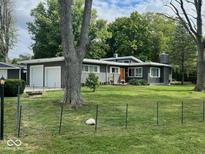 Charming single-story home featuring a well-manicured lawn, two-car garage, orange front door, and mature trees at 6805 Twin Brooks Dr, Indianapolis, IN 46227