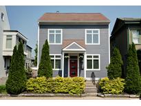 Charming two-story home featuring gray siding, complemented by lush green landscaping and a vibrant red front door at 1021 N Alabama St, Indianapolis, IN 46202