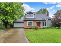 Charming front exterior featuring a brick facade and inviting red door, with mature trees and a lush lawn at 7430 Railway Ct, Indianapolis, IN 46256