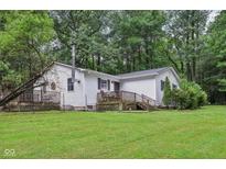 View of the home's exterior with a deck overlooking a lush green yard surrounded by mature trees at 2640 S Silcox Rd, Paragon, IN 46166