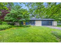 Charming single-story home with stone and blue siding, mature trees, a yellow front door and a well-manicured front lawn at 6704 Hoover Rd, Indianapolis, IN 46260