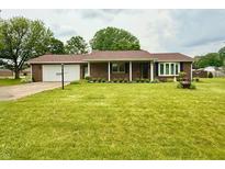 Charming brick home featuring a well-manicured lawn, attached garage, and decorative landscaping at 9099 Ne Oak St, Alexandria, IN 46001