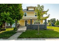 Inviting yellow two-story home with a classic design, showcasing a lush green lawn and mature trees at 805 N Temple Ave, Indianapolis, IN 46201