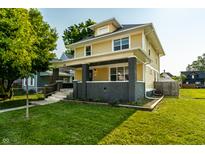 Charming yellow two-story home featuring a covered porch and a well-manicured front lawn on a sunny day at 805 N Temple Ave, Indianapolis, IN 46201