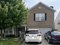 Two-story brick home featuring a front lawn, attached garage, and cars parked in the driveway at 12509 Teacup Way, Indianapolis, IN 46235