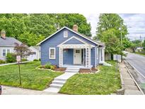 Charming blue home with a covered front porch, complemented by green grass and mature trees at 5203 Carrollton Ave, Indianapolis, IN 46220