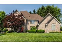 Charming brick home with a well-manicured lawn, lush trees, and a vibrant red front door at 1229 Helford Ln, Carmel, IN 46032