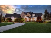 Stunning stone home with lush lawn, covered porch, and circular driveway at dusk at 13346 W Sherbern Dr, Carmel, IN 46032