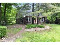 Charming log cabin with a red door surrounded by a lush green yard and mature trees at 20417 State Road 37 N, Noblesville, IN 46060