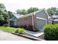 Charming home featuring brick accents, attached garage, manicured lawn, and vibrant flowering shrubbery at 8023 Talliho Dr, Indianapolis, IN 46256