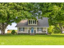 Charming tan farmhouse-style home with a covered front porch and lush green lawn and mature trees at 14855 E State Road 46, Columbus, IN 47203