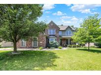 Charming two-story brick home with a well-manicured lawn and mature trees on a sunny day at 1808 Woodfield Dr, Greenwood, IN 46143