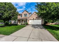 Traditional brick home with a well-manicured lawn, long driveway, and mature trees under a blue sky at 9740 Logan Ln, Fishers, IN 46037