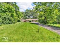 Inviting single-story home featuring an expansive green lawn, mature trees, and a private driveway at 450 W 93Rd St, Indianapolis, IN 46260