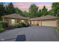 Brick house featuring an attached garage, asphalt driveway, and tasteful landscaping under a vibrant sky at 7029 Kingswood Cir, Indianapolis, IN 46256